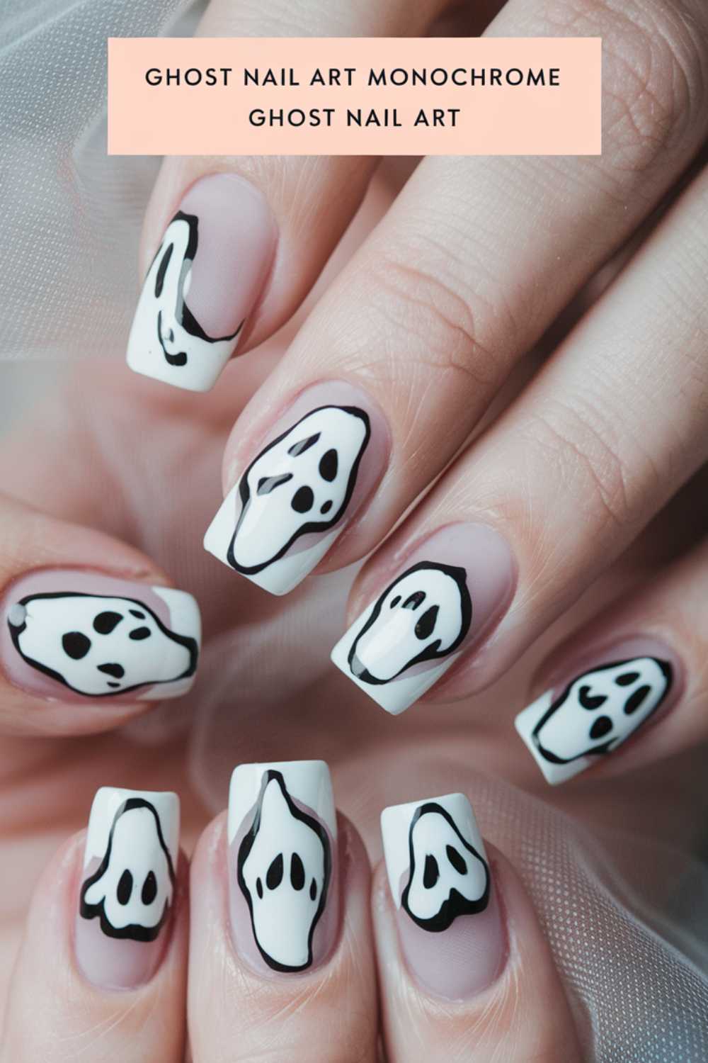 Close-up of hands with monochrome ghost nail art on square-shaped nails. The design features black and white ghost faces on a matte white background, with a soft sheer fabric in the background.