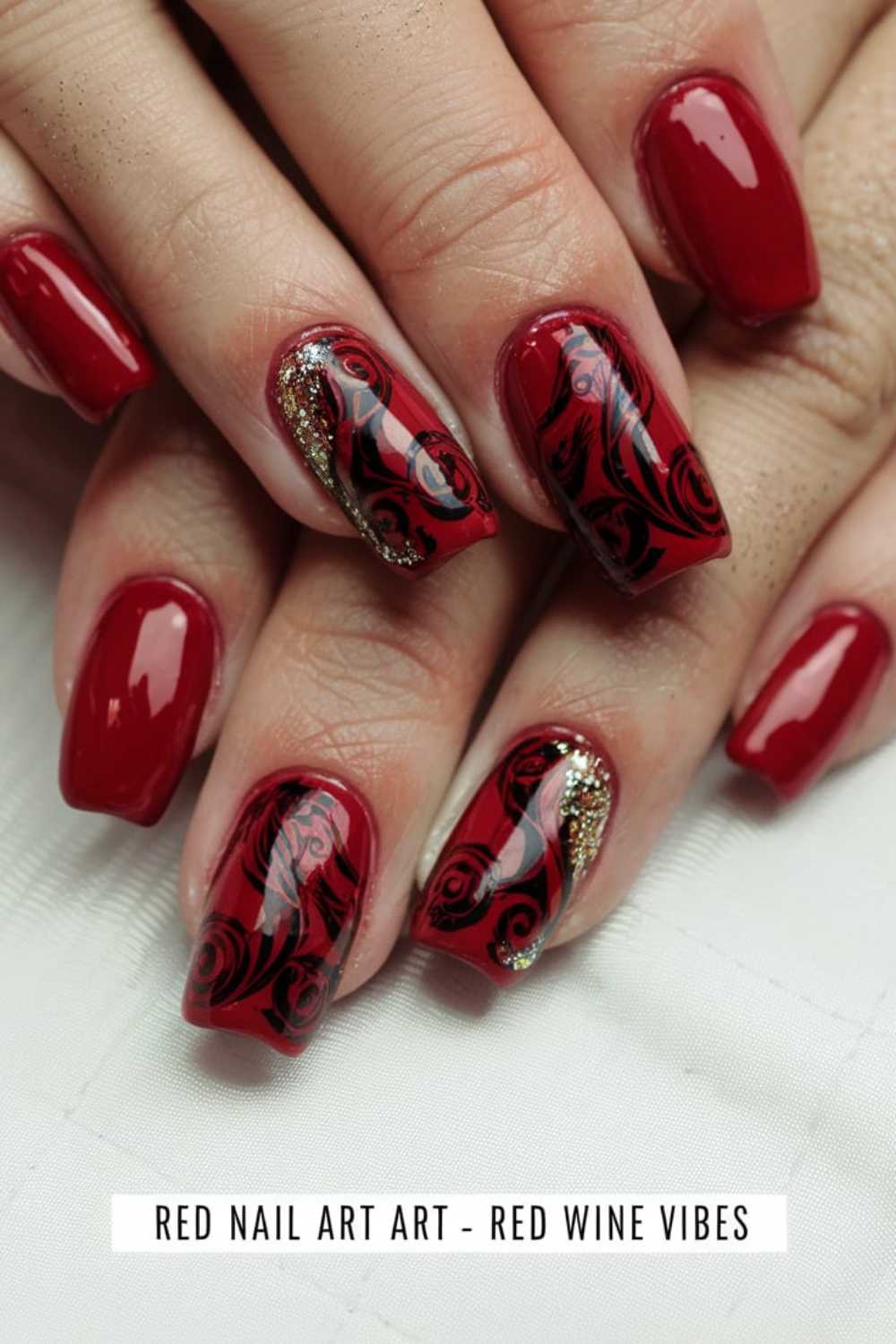 Close-up of hands with glossy, blood-red nails. Two nails on each hand feature black swirl accents and gold glitter details. The caption reads Red Nail Art Art - Red Wine Vibes.