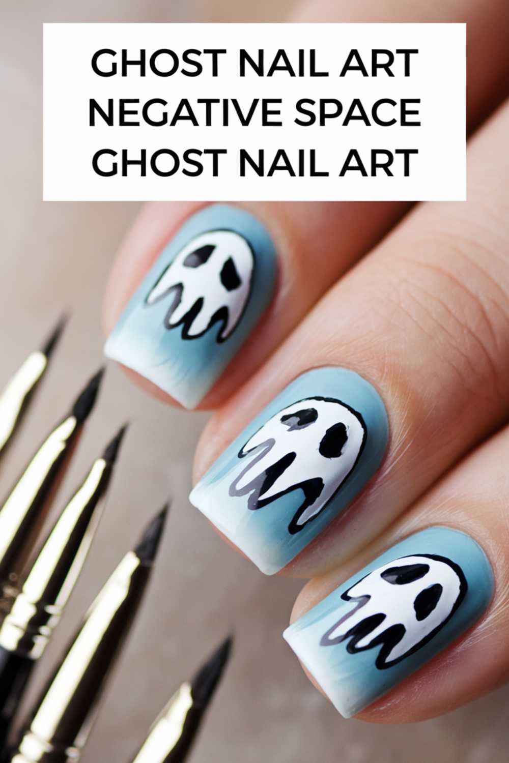 Close-up of nails with ghost-themed nail art, featuring black and white ghost designs on a gradient blue background. Several fine-tipped brushes are visible beside the nails. Text above reads: Ghost Nail Art Negative Space Ghost Nail Art.