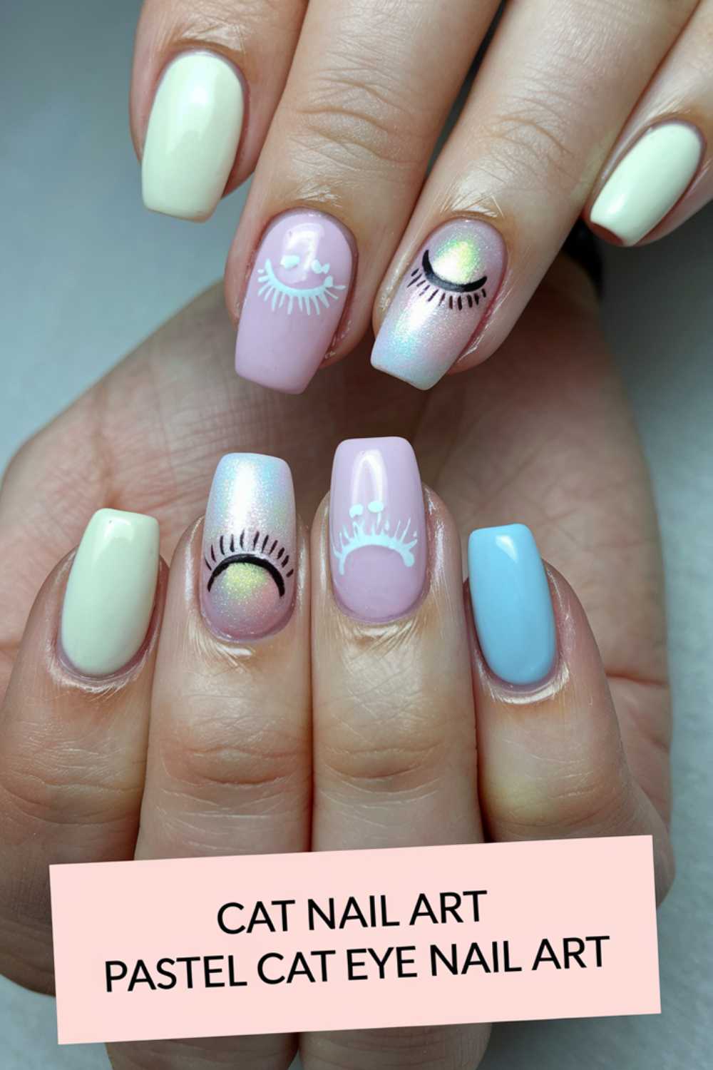 Close-up of a hand with pastel-colored nails displaying cat eye designs. The nails are painted in light yellow, pink, and blue, with some nails featuring eye shapes with eyelashes. A text overlay reads, Cat Nail Art Pastel Cat Eye Nail Art.