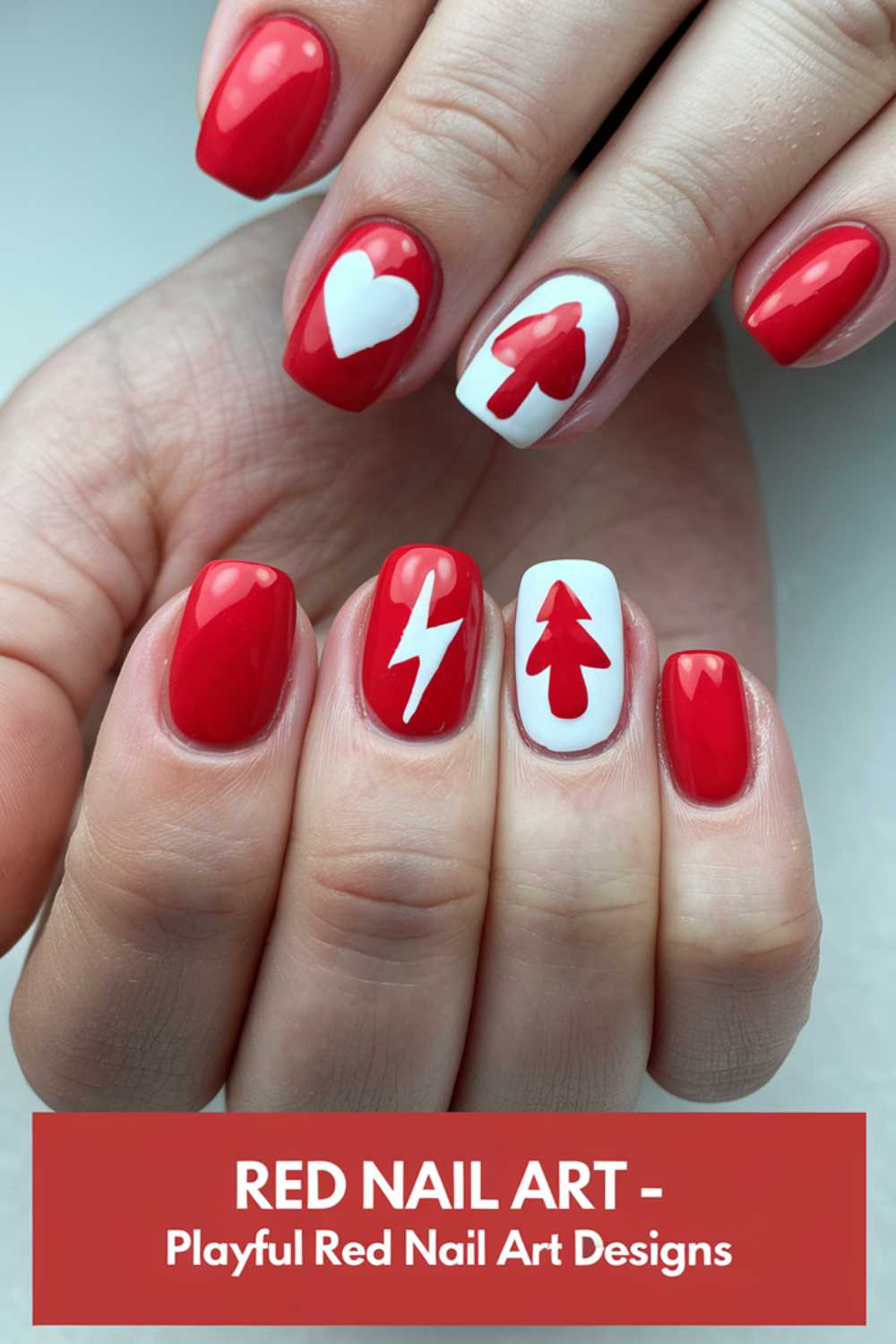 Close-up of hands displaying red nail art. Designs include white shapes: a heart, lightning bolt, arrow, and tree on accent nails. Text at the bottom reads, Red Nail Art - Playful Red Nail Art Designs.
