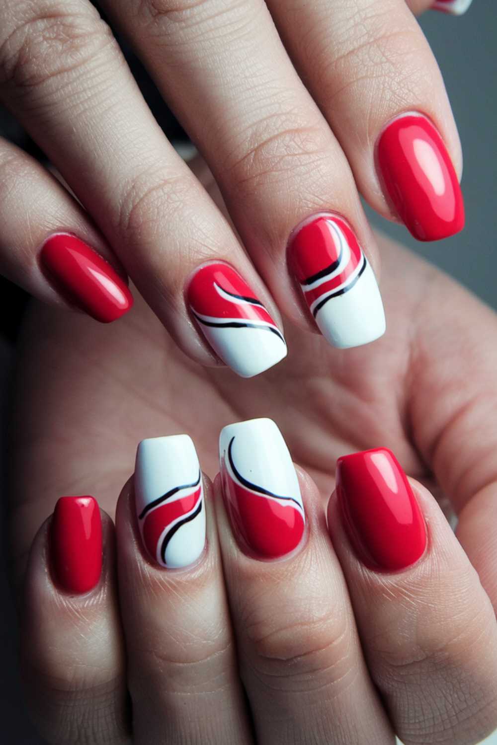 Close-up of hands with red and white nails. The middle and ring fingers feature abstract red, white, and blue swirl designs, while the other nails are solid red. The design is glossy and vibrant.
