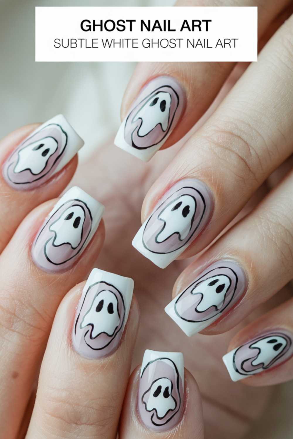 Close-up of hands with nails featuring ghost nail art. The design includes white ghost shapes with black eyes and mouths on a light, nude background. Each nail has a distinct ghost face, creating a playful, spooky theme. Text reads: Ghost Nail Art.
