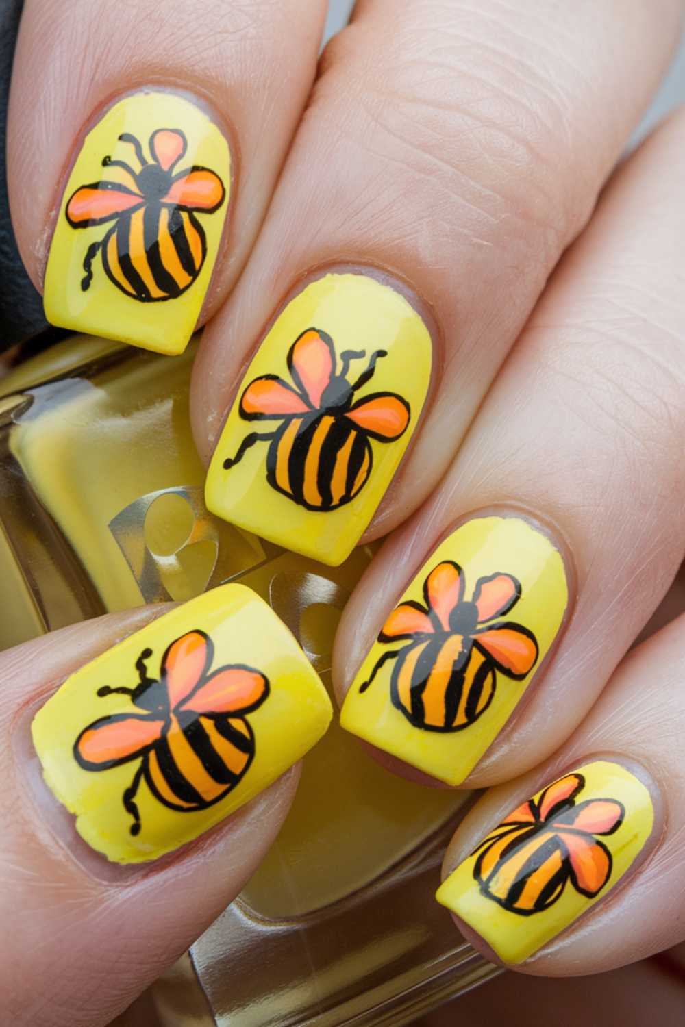 Close-up of Bee Nail Art showcasing fingernails painted with bright yellow polish, each adorned with a detailed black and orange bee design. The bees feature black stripes and translucent wings, beautifully set against the sunny backdrop.