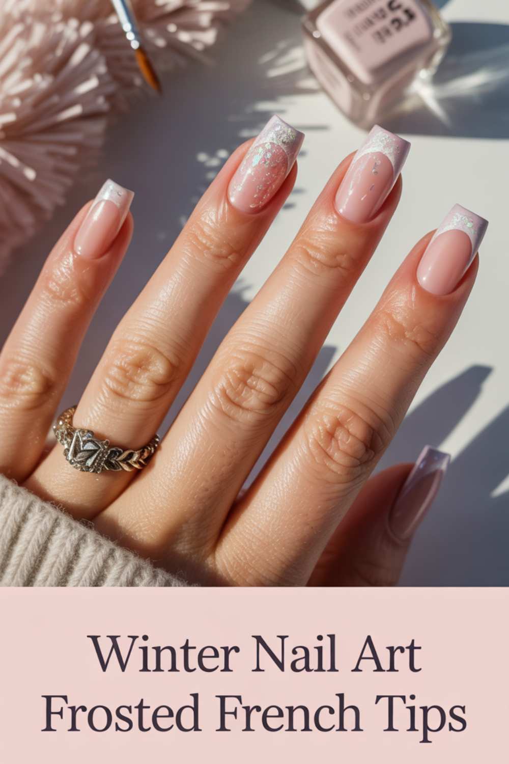 A hand with square-shaped nails featuring frosted French tips and subtle white nail art, shown holding a sweater sleeve. Text reads: Winter Nail Art Frosted French Tips.
