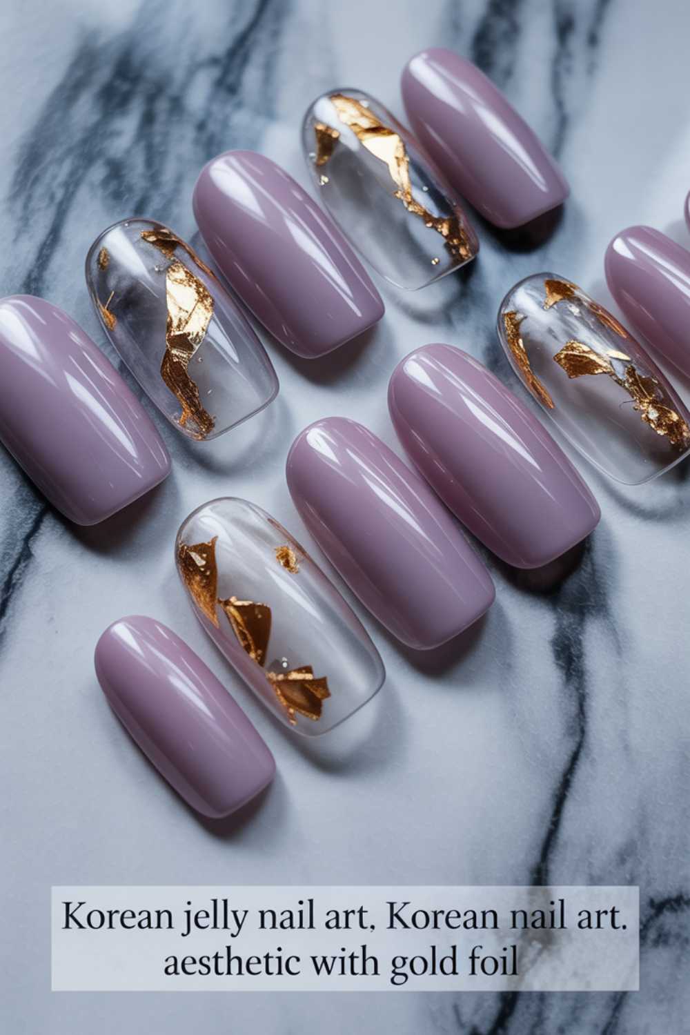 A set of press-on nails featuring a Korean jelly nail art design in mauve and clear polish with gold foil accents, displayed on a marble surface.