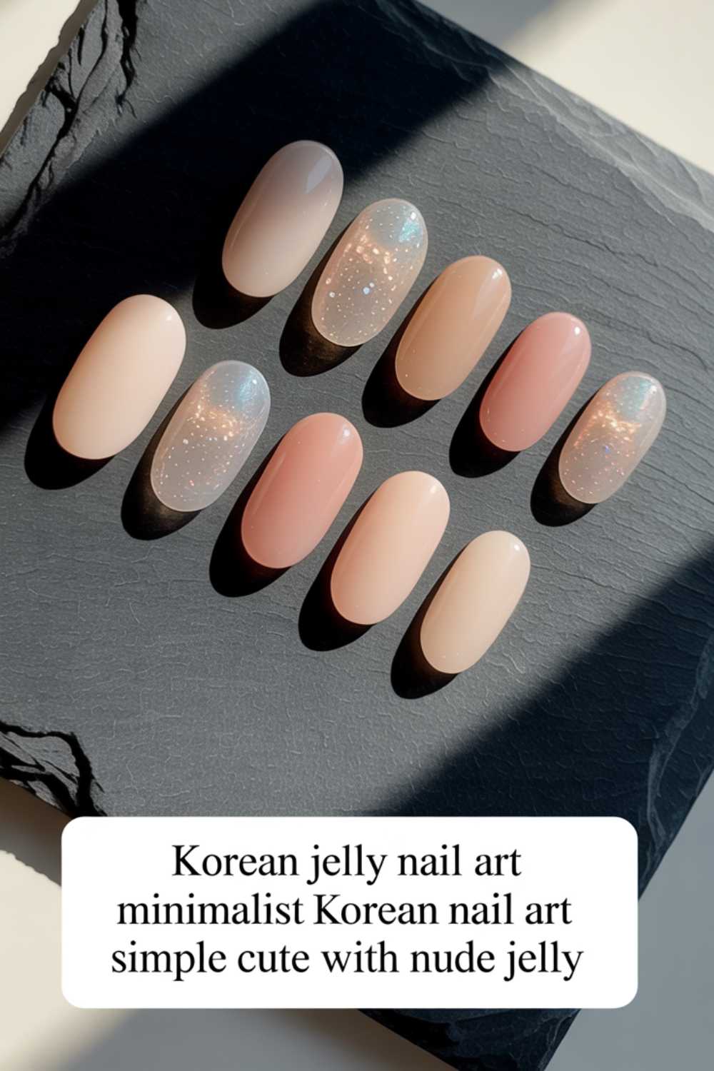 A set of ten artificial nails in nude and jelly shades with subtle glitter, arranged on a black slate. A caption below reads: Korean jelly nail art minimalist Korean nail art simple cute with nude jelly.