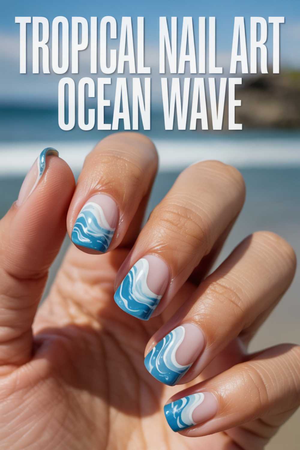 A hand with square-shaped nails featuring tropical ocean wave nail art in blue and white, with a beach and sea blurred in the background. Text reads, Tropical Nail Art Ocean Wave.
