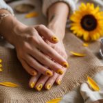 A pair of hands with sunflower-themed nail art rest on burlap surrounded by sunflower blooms, petals, and bottles of nail polish on a beige fabric surface.