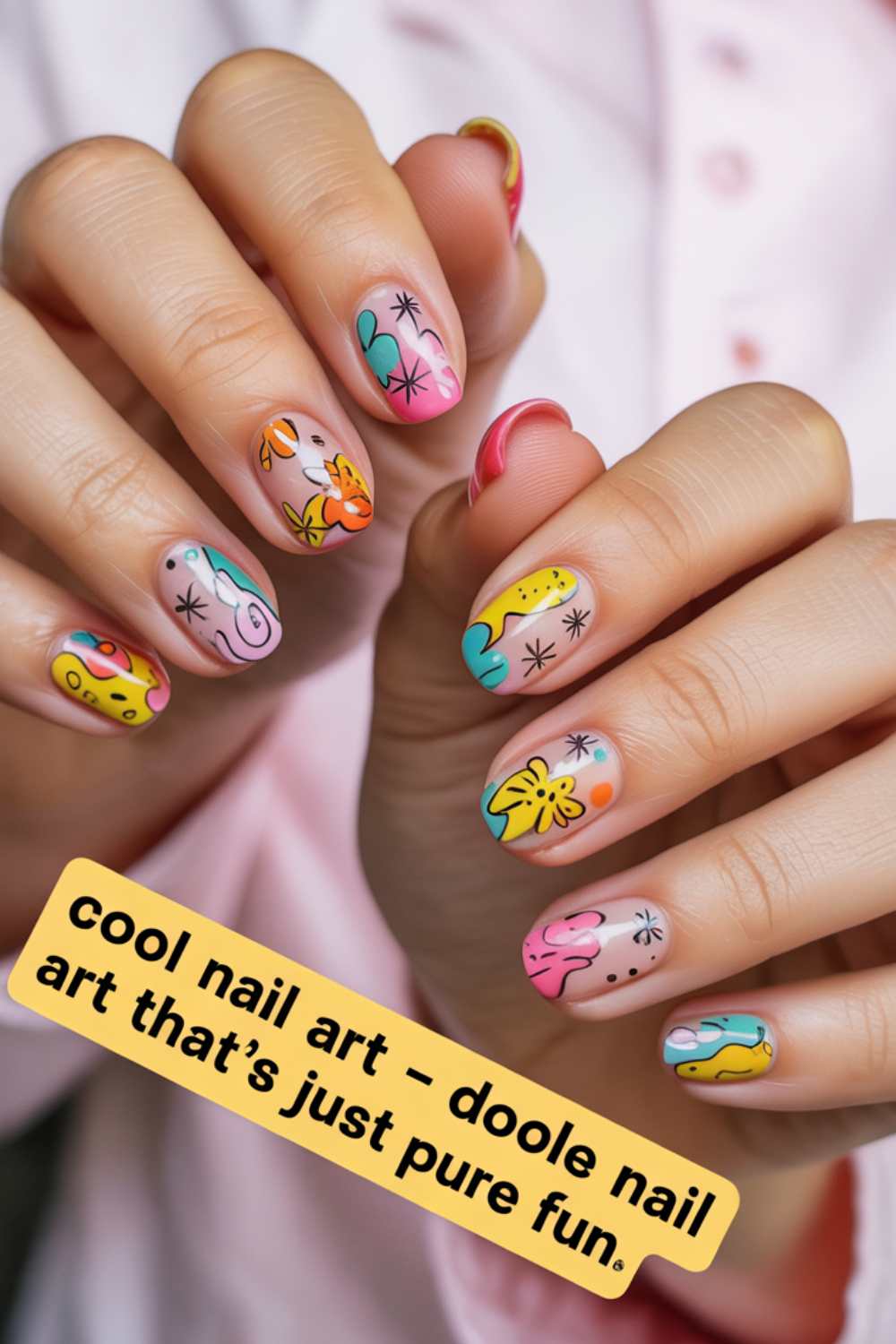 Close-up of hands with colorful doodle nail art featuring playful abstract designs. A yellow caption reads, “cool nail art – doodle nail art that’s just pure fun.” Person wears a light pink shirt in the background.