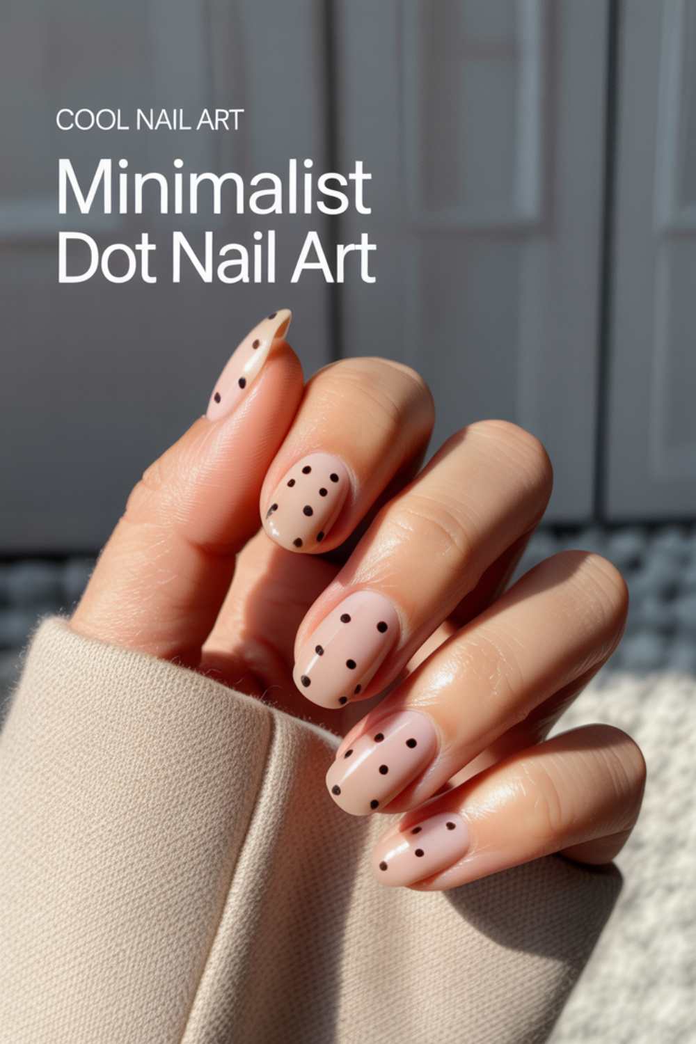 A hand with long almond-shaped nails featuring minimalist black dot nail art on a nude base. The text overlay reads, Cool Nail Art, Minimalist Dot Nail Art. The person is wearing a beige sleeve.